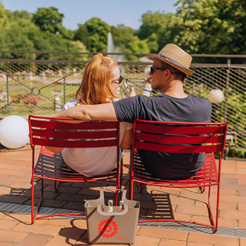 Ein Paar sitzt einander gegenüber auf roten Stühlen im Freien und genießt an einem sonnigen Tag Getränke.